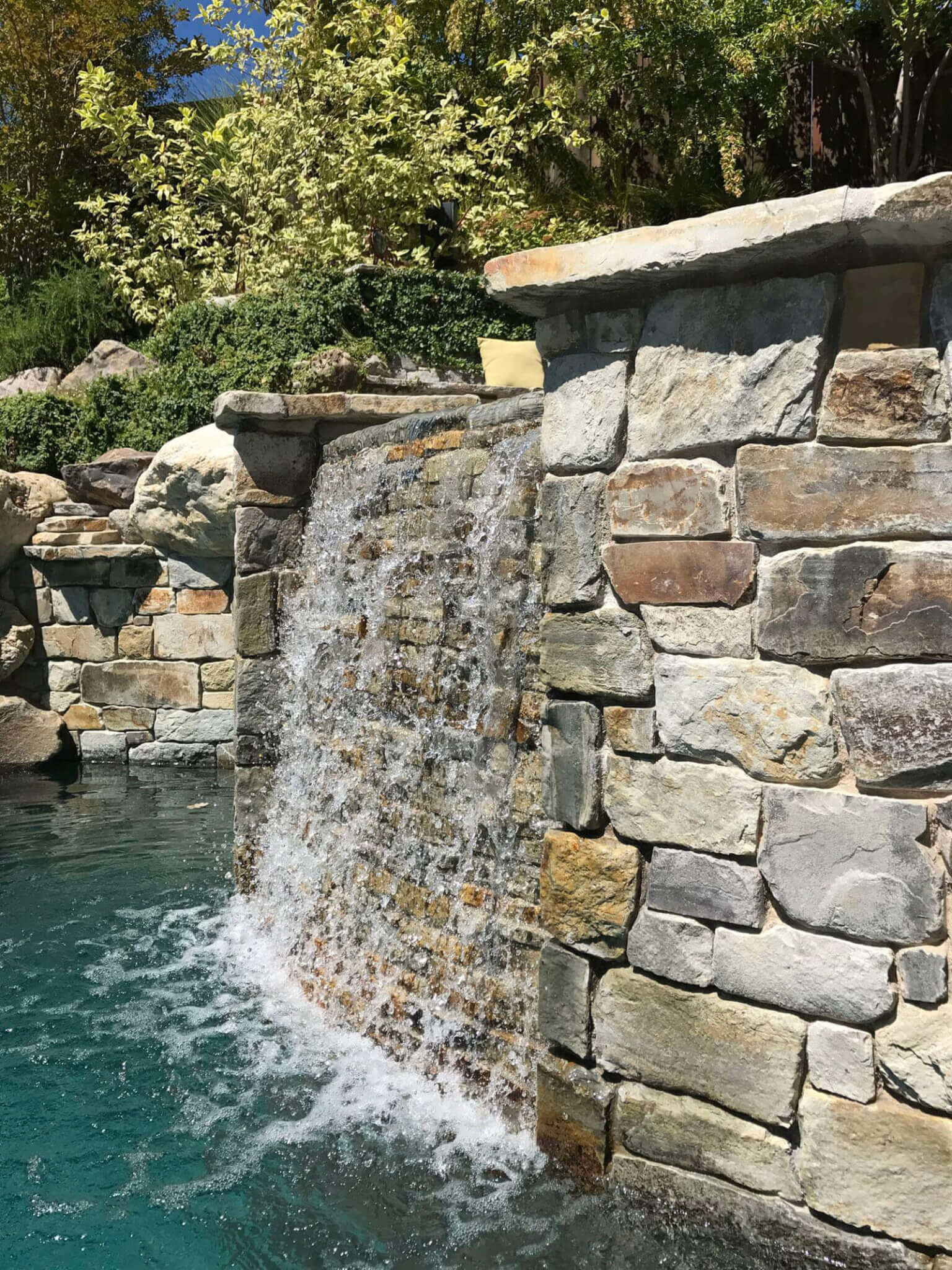 Rock walled elevated jacuzzi with water wall flowing into lower pool area