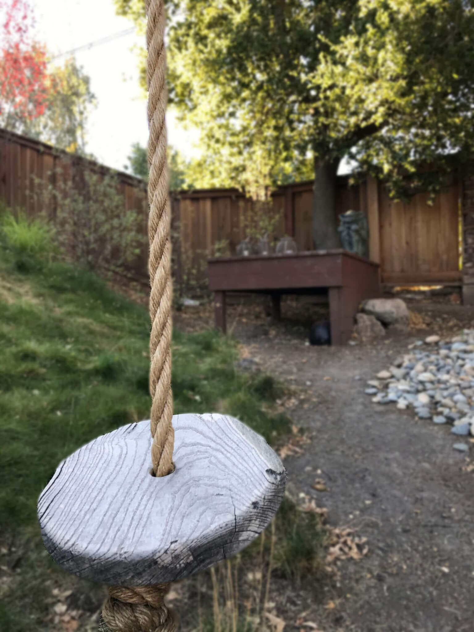 gray seated rope swing waiting to be ridden in slightly sloped yard