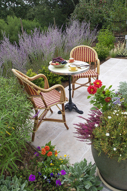 Colorful flowers surround a patio table and chairs in this eclectic cottage garden