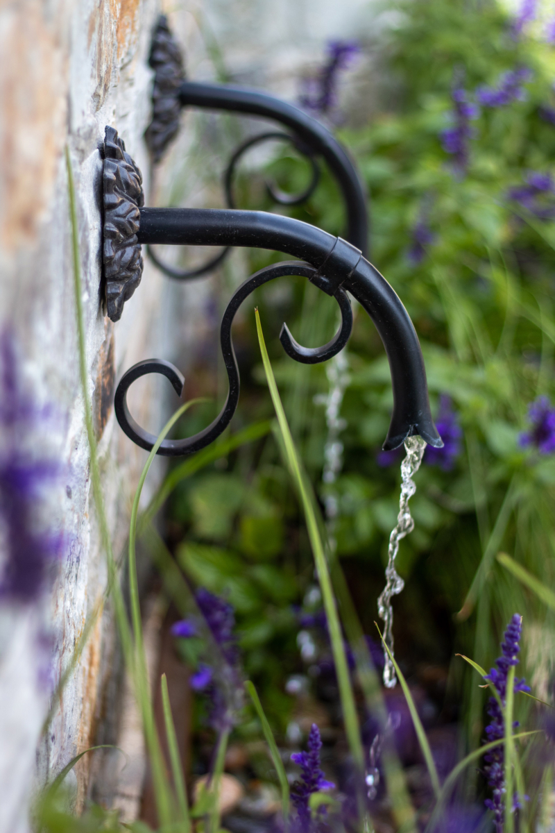 Delicate metal spouts of traditional fountain pour among planted border