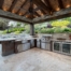 Custom stone and wood pavilion shades outdoor kitchen with grill, sink, storage and drinks fridge