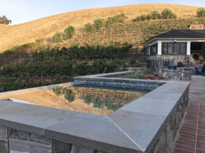 Infinity-edge reflecting pool with golden hills and vineyard in Sonoma-style landscape