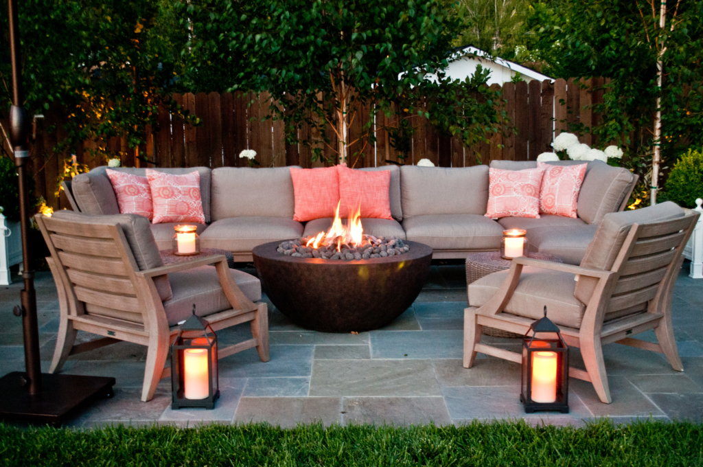 Rose-colored accents and cozy patio furniture surround a fire bowl