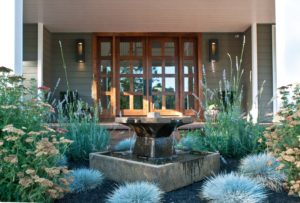 Square Chinese-style fountain surrounded by calming garden planting creates a focal point before a contemporary front door of wood and glass