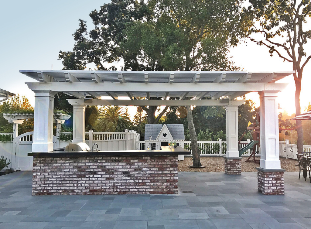 Outdoor kitchen under a white contemporary pergola with brick post accents