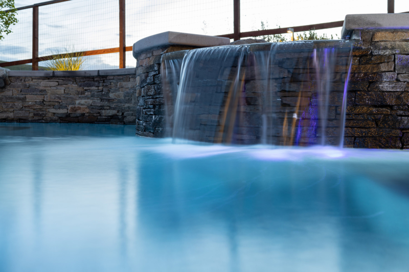 Cascading waterfall from elevated spa into pool below with violet LED lighting
